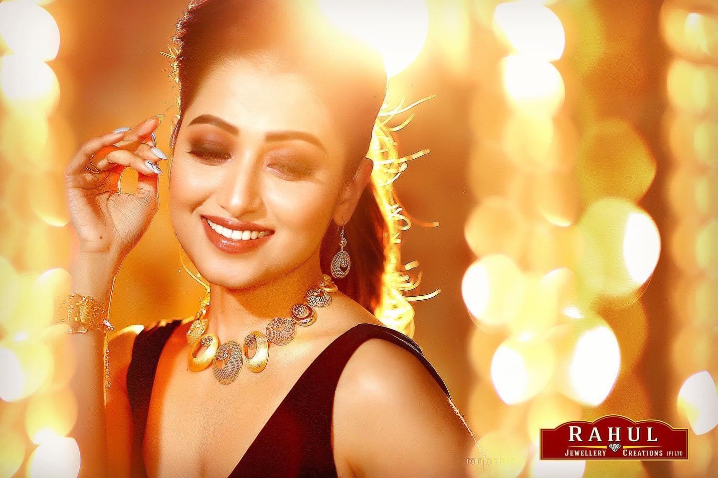 Elegant portrait of actress Sudipta Banerjee for Rahul Jewelers ad campaign by Ranjan Bhattacharya Photography. The actress is smiling while showcasing exquisite jewelry against a golden bokeh background.