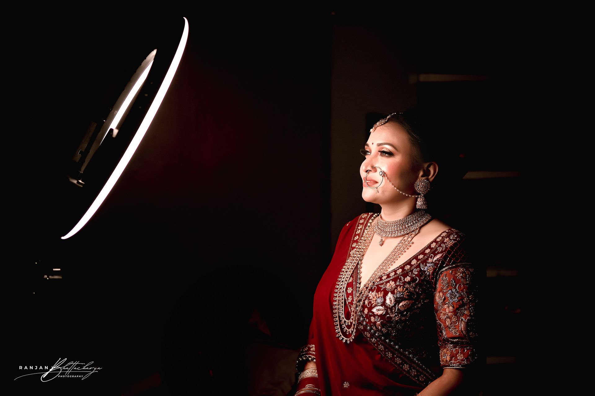 Ruhi Singh, dressed in a rich maroon bridal outfit, illuminated by a soft ring light, ready for her bridal portrait, captured by photographer Ranjan Bhattacharya.