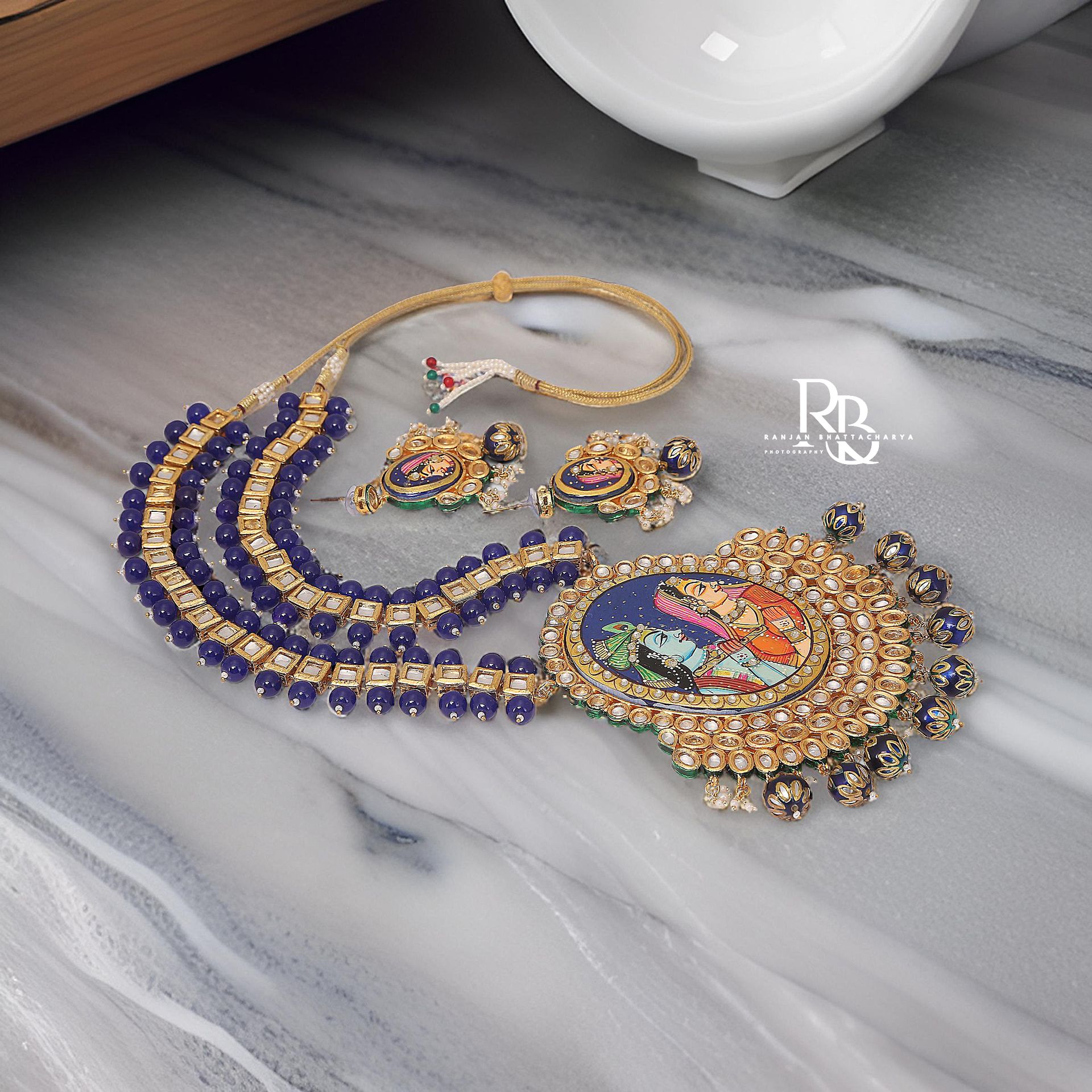 Handcrafted necklace and earrings set with Krishna & Radha Pichwai art and blue bead embellishments, photographed by Ranjan Bhattacharya.