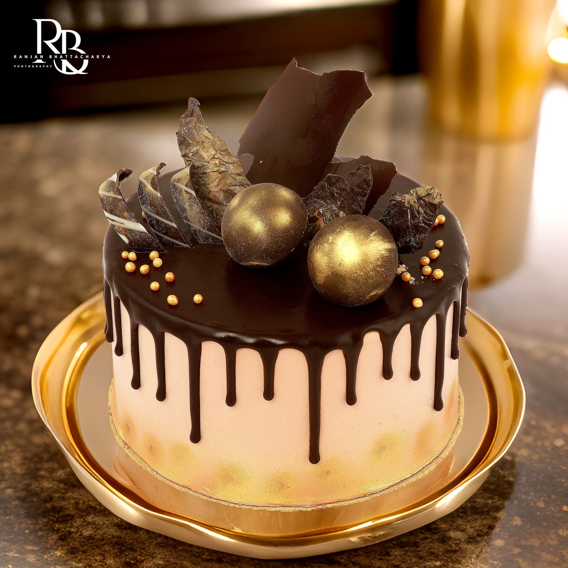 A beautifully decorated cake with chocolate drip and golden accents, featuring artistic chocolate decorations on top, captured by Ranjan Bhattacharya Photography for The Sugarr & Spice.