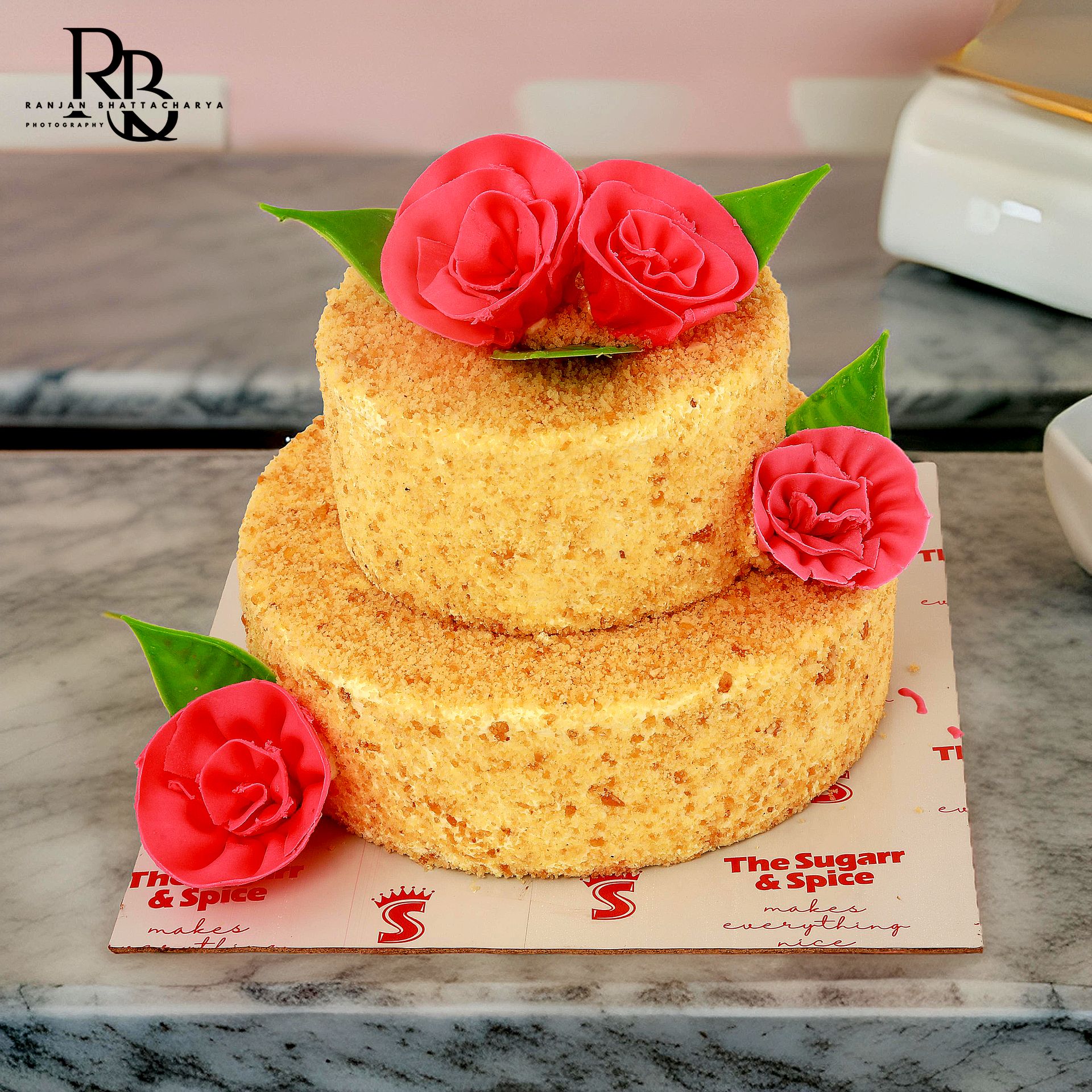 Elegant cake adorned with two red roses, captured in stunning product photography for "The Sugarr and Spice" by Ranjan Bhattacharya.