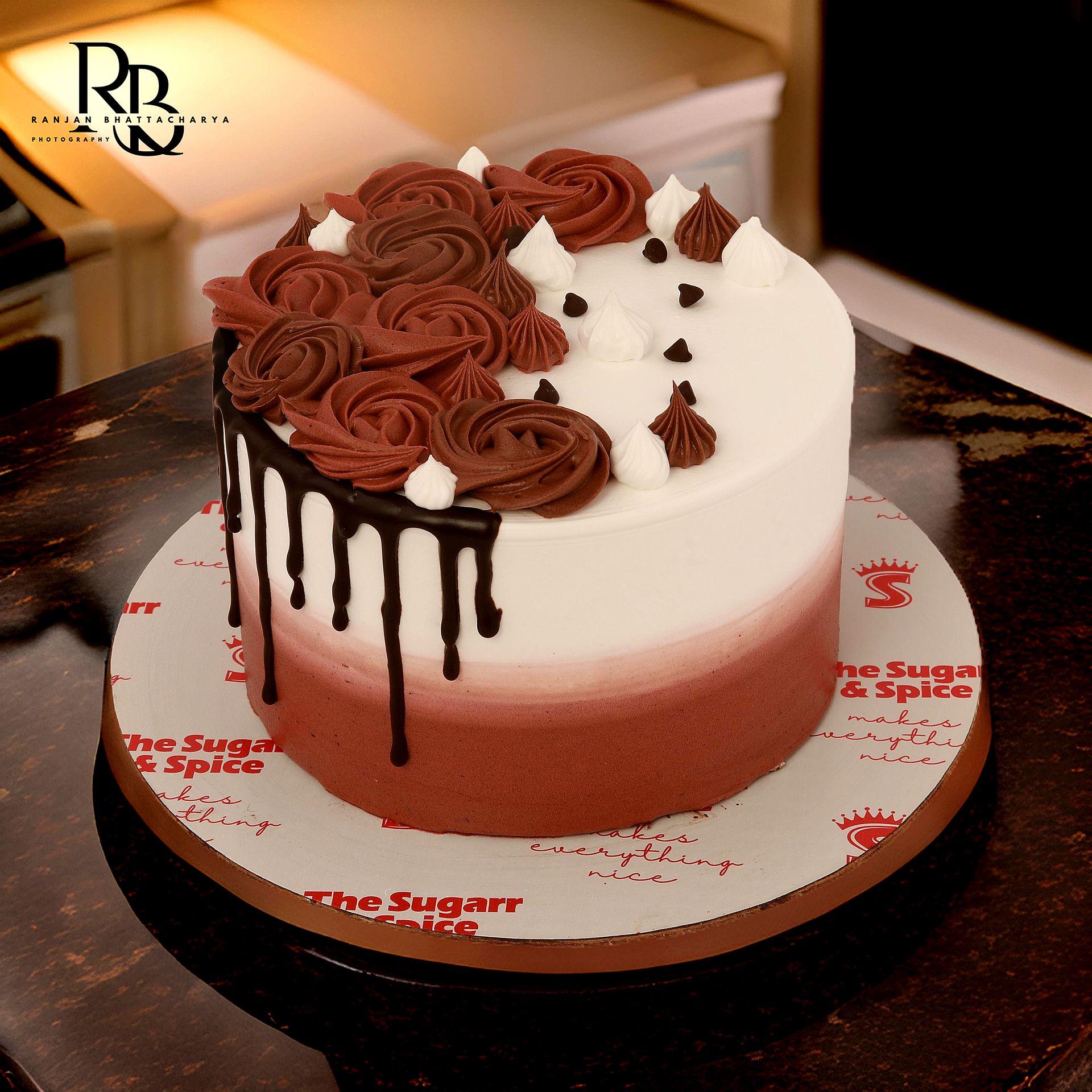 An exquisite cake with vibrant red and white icing and drips, presented in product photography for "The Sugarr and Spice."