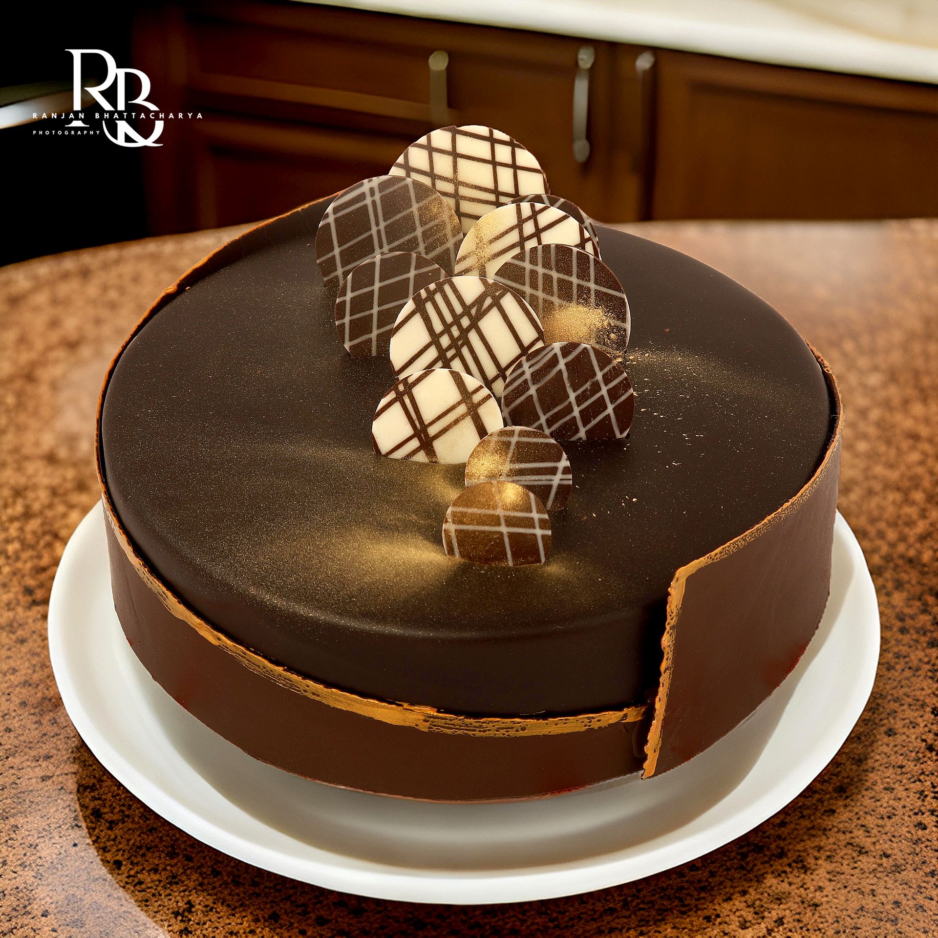 A luxurious chocolate cake featuring a chocolate piece on top, elegantly photographed for "The Sugarr and Spice" by Ranjan Bhattacharya.