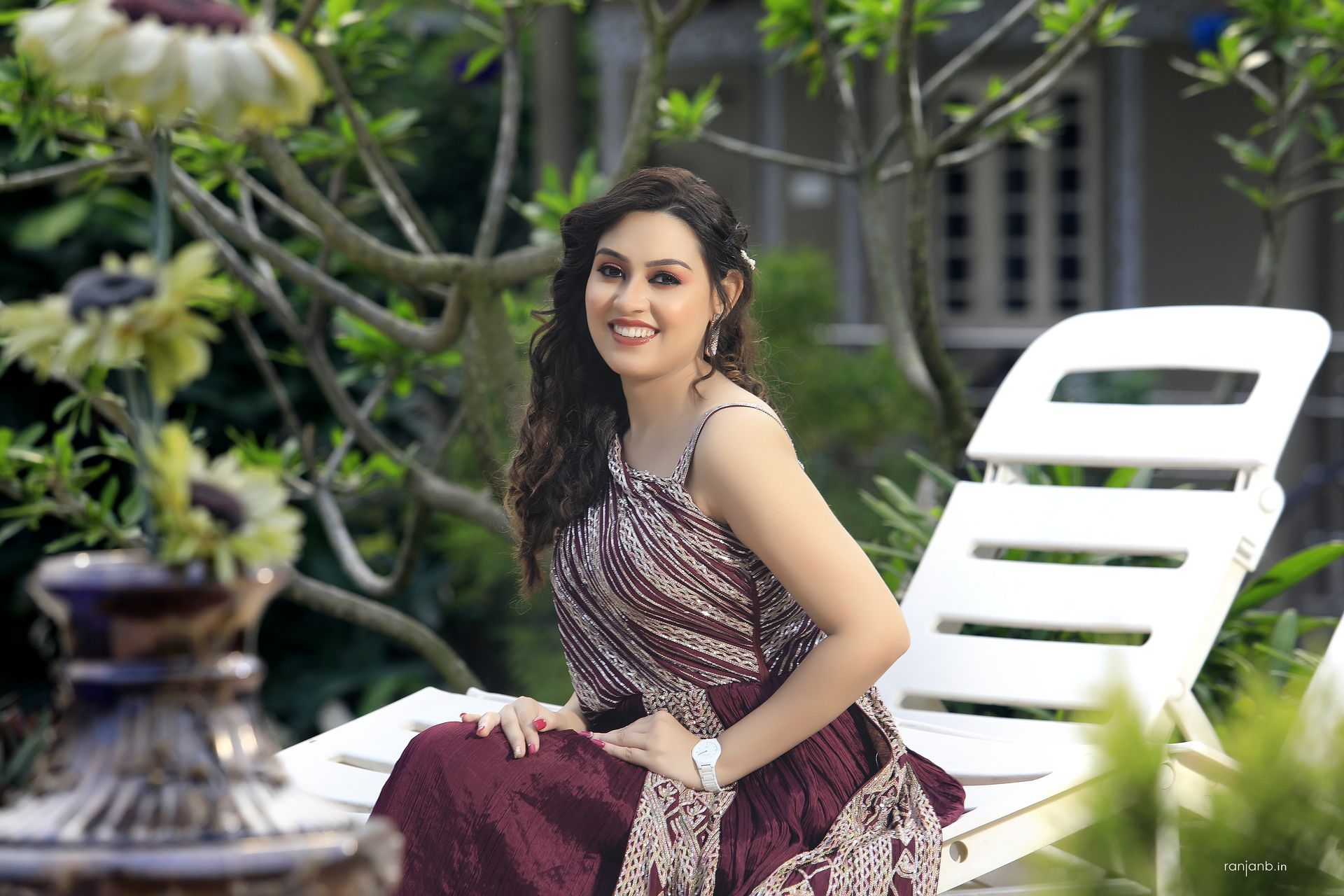 Elegant portrait of a lady in a maroon dress seated outdoors, captured by Ranjan Bhattacharya, showcasing natural beauty and serene environment.