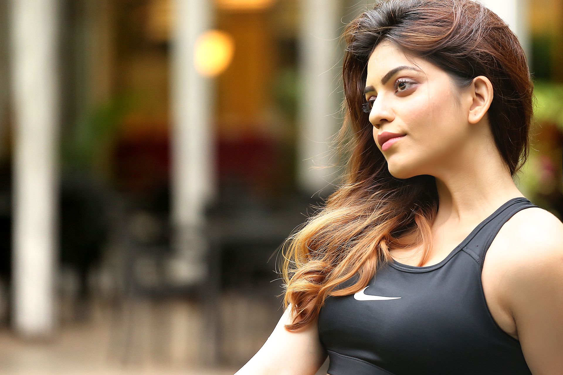 A candid portrait of Monisha Sen by Ranjan Bhattacharya Photography, captured from behind. She wears a black Nike tank top, her long brown hair flowing. The softly blurred outdoor background adds depth and warmth.