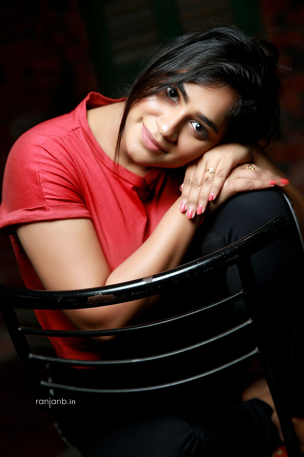 Casual portrait of a young woman in a red t-shirt, smiling while sitting on a chair, photographed by Ranjan Bhattacharya.