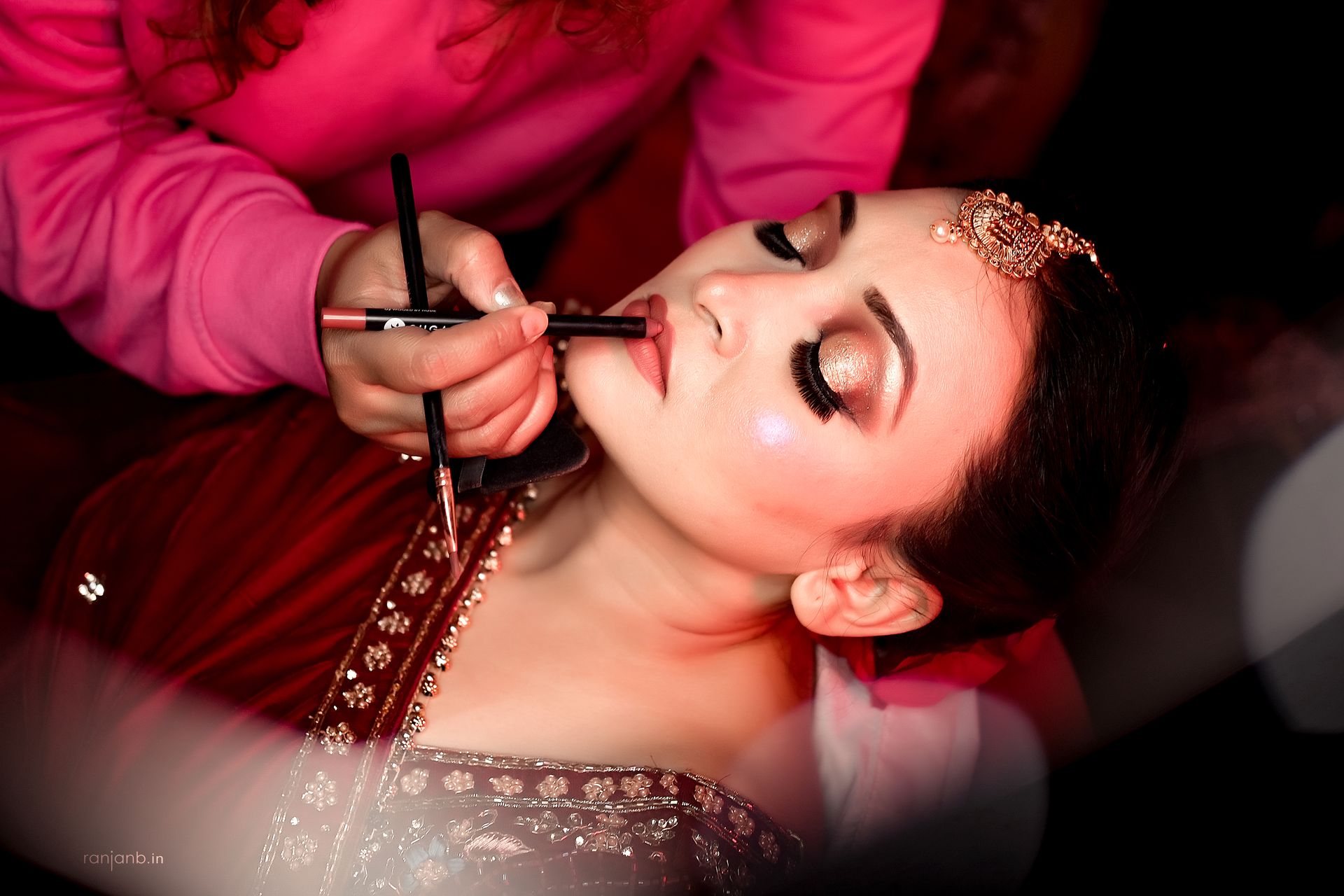 Close-up shot of Ruhi Singh having her makeup applied, photographed by Ranjan Bhattacharya, showcasing her glittery eyeshadow and traditional bridal attire.